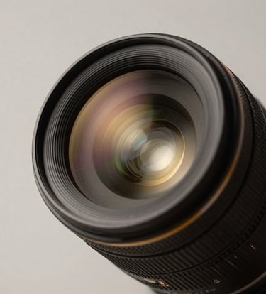 A close-up shot of a high-end professional camera lens reflecting a soft off-white studio light in a Turkish / Istanbul photography studio. Minimalist composition with deep charcoal black and metallic warm gold highlights.