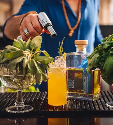 a man is making a uno tequila cocktail at a bar with a bottle of uno tequila añejo