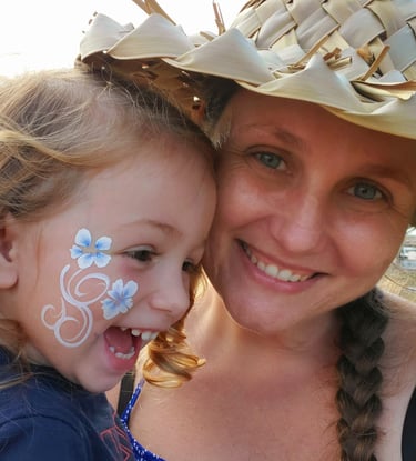 a woman with a hat on her head holding a smiling little girl with a flowers painted on her cheek