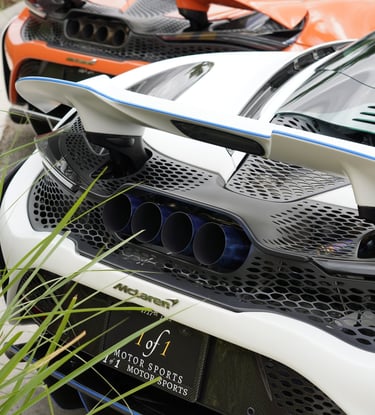Rear view of white and orange McLaren 765LT supercars featuring titanium exhaust tips and carbon fiber wings.