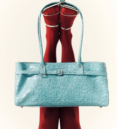 Light blue faux crocodile skin handbag held up by legs wearing red tights and silver heels.