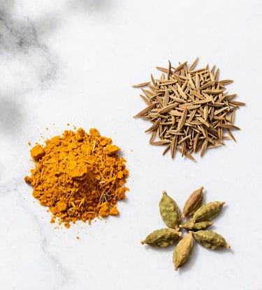 Bright overhead flat-lay of turmeric, cumin, and cardamom on a clean white marble background with soft natural daylight.
