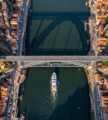 Aerial view of luxury yacht passing under historic Douro River bridge in Porto at golden hour.