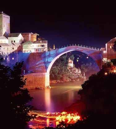 Mostar Old Bridge lit with colorful lights reflecting on Neretva River at night