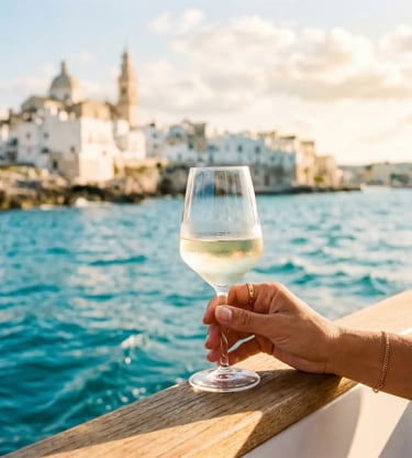 Hand holding white wine glass on boat with Monopoli skyline behind