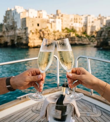 Couple toasting with chilled prosecco glasses on boat deck with Polignano a Mare cliffs behind