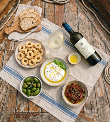 Overhead flat-lay of burrata, taralli, olives, sun-dried tomatoes and Puglia white wine on boat deck