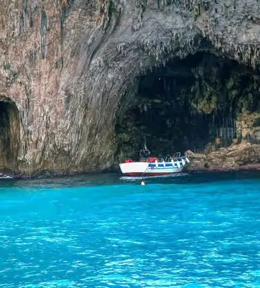 Tour boat anchored inside limestone sea cave with turquoise water on Salento coast near Otranto