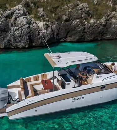 Modern private boat anchored in crystal turquoise water beside limestone cliffs in Salento