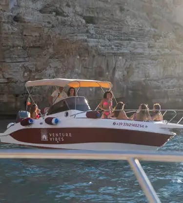 Group enjoying Monopoli boat tour with shaded canopy near limestone cliffs at sunset