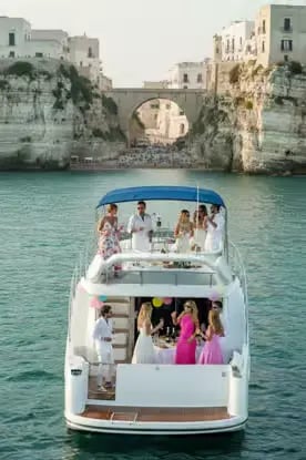 Guests enjoying Apulian aperitif party on luxury yacht beneath dramatic Polignano a Mare cliffs