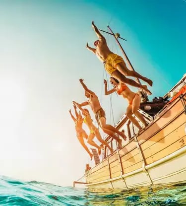 Group of guests jumping from a traditional wooden boat into turquoise Mediterranean sea water