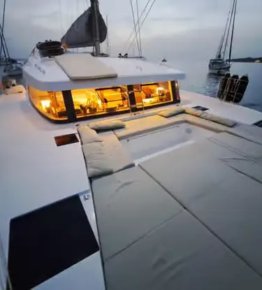 Luxury catamaran foredeck with cushions and warm cabin lights at dusk in Menorca