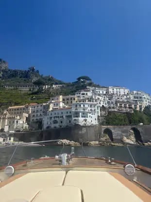 View of Amalfi town white buildings on hillside from the bow of a Gozzo boat on a sunny day