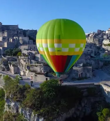Green and yellow hot air balloon floating above the ancient Sassi di Matera stone houses and canyon