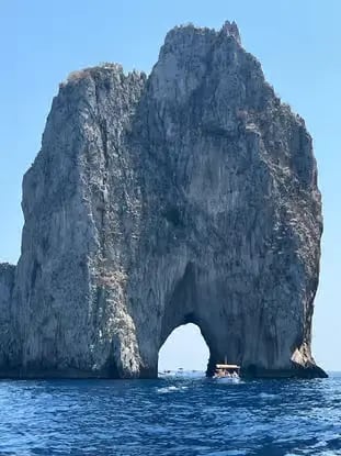 Small boat passing through the natural arch of the Faraglioni rocks on Capri private boat tour.