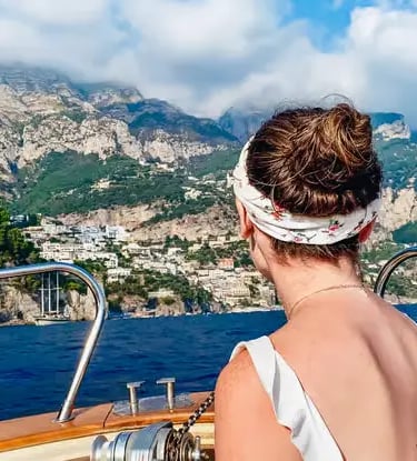 Woman on a Gozzo boat deck gazing at the Positano cliffside village from the sea
