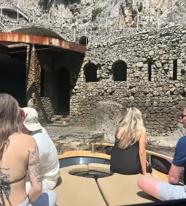 Guests on small boat approaching hidden stone sea cave along Golfo del Pecoriello in Capri