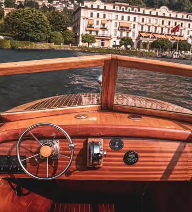 Vintage wooden boat cockpit steering toward historic villa on Lake Como