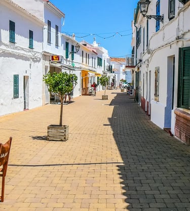 Sun-drenched whitewashed street with green shutters and string lights in Menorca, Spain