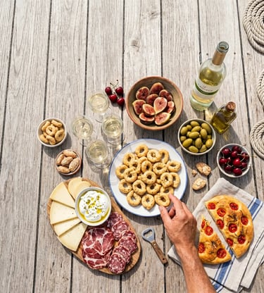 Overhead view of taralli, burrata, figs, salumi and white wine on wooden boat deck