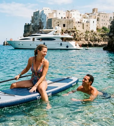 Smiling couple on SUP paddleboard next to luxury yacht in turquoise water of Polignano a Mare