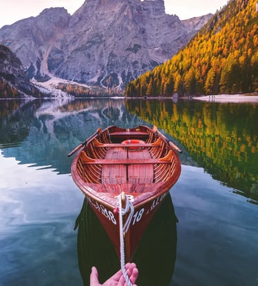 Hand holding rope of wooden rowboat on Lake Braies with autumn Dolomite reflections