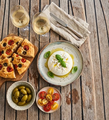 Overhead view of burrata, focaccia, olives, tomatoes and white wine on teak boat deck