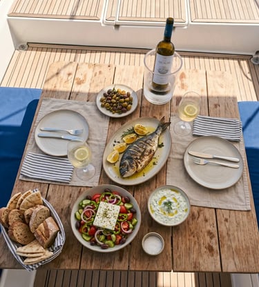 Fresh Greek lunch with grilled fish, salad, olives and white wine served on catamaran deck.