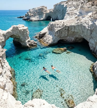 Two swimmers in crystal-clear turquoise water between white rock arches at Kleftiko, Milos, Greece