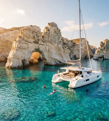 White luxury catamaran anchored at Kleftiko cliffs in Milos with swimmers in turquoise water.
