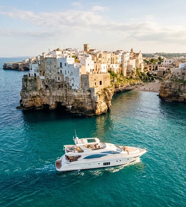 White luxury yacht sailing past Polignano a Mare cliffs and old town on turquoise Adriatic sea