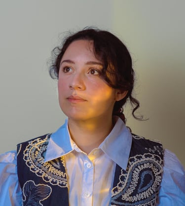 A young woman wearing an embroidered vest over a white blouse with artistic lighting.