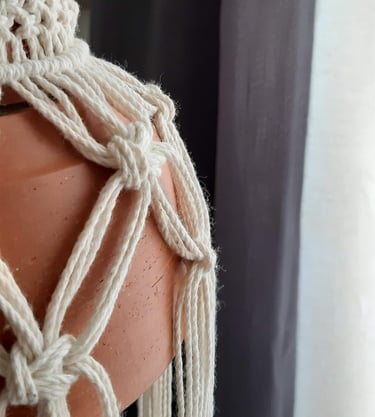 Primer plano de un tejido de macramé blanca que sostiene una lámpara de barro