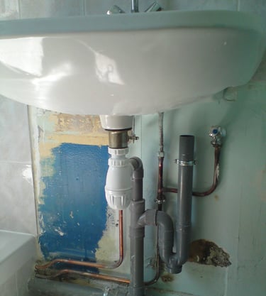 Installation complète de la plomberie sous un lavabo : siphon, tuyaux d’évacuation et raccords cuivr