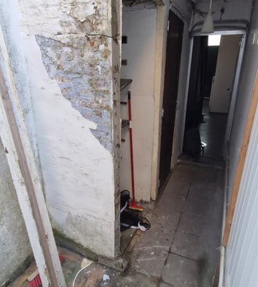 Couloir intérieur en cours de démolition avec murs dégradés, plafond effondré et traces d’humidité.