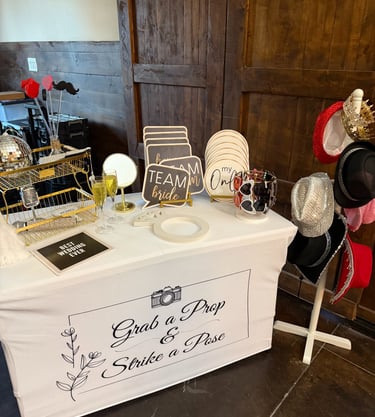 Wedding photo booth prop station with signs, hats, and glasses on a white table.