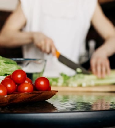 Femme coupant des légumes sur une planche avec des légumes frais au premier plan