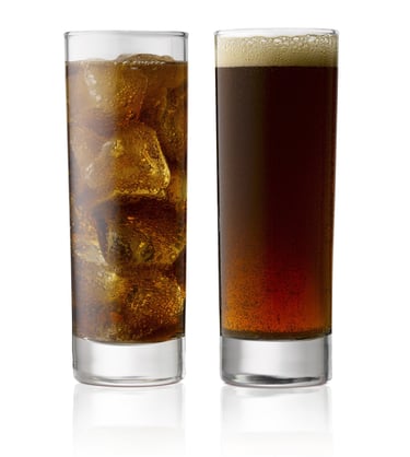 two glasses of coke side by side one with ice one without on a white reflective background