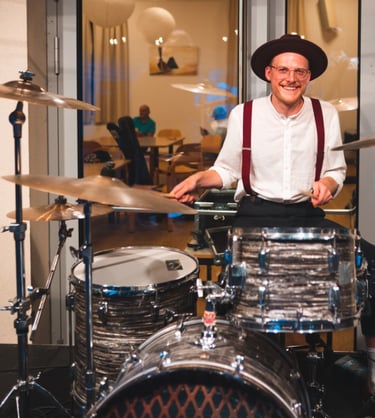 a man in a hat and suspenders playing drums