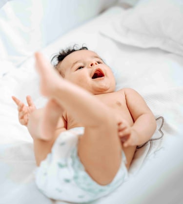 Smiling baby lying on bed – natural newborn photography by Fred Art Studio London