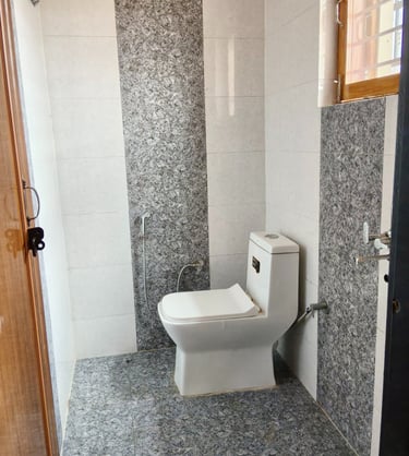Modern bathroom featuring a white ceramic toilet and grey granite wall and floor tiling.