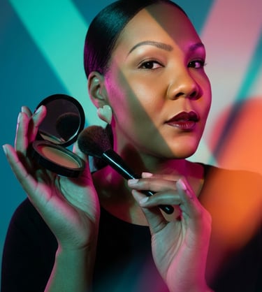 A woman applying make-up with a brush and powder compact under colorful neon lighting.