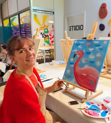 Une femme souriante peint un flamant rose sur une toile lors d’un atelier in strasbourg