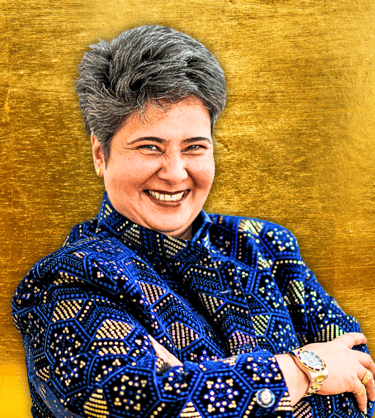 Indian woman with crossed arms smiling at camera, She is wearing a royal blue jacket with gold.