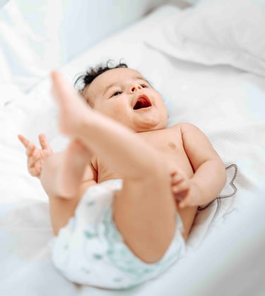 Smiling baby lying on bed – natural newborn photography by Fred Art Studio London