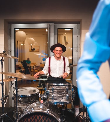 a man in a hat and suspenders playing drums