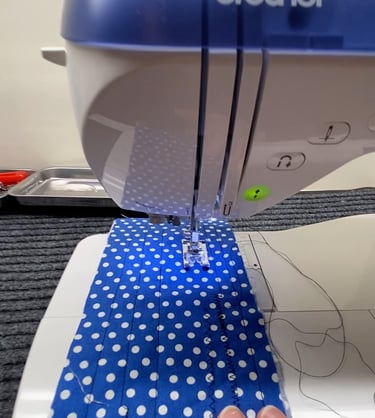 A hand feeding blue polka-dot fabric through the needle and foot area of a sewing machine.