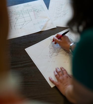 A female engineer sketching detailed technical drawings and blueprints on a dark wooden desk.