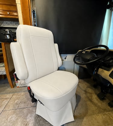 Luxury white leather captain's chair inside a motorhome RV cockpit next to the steering wheel.